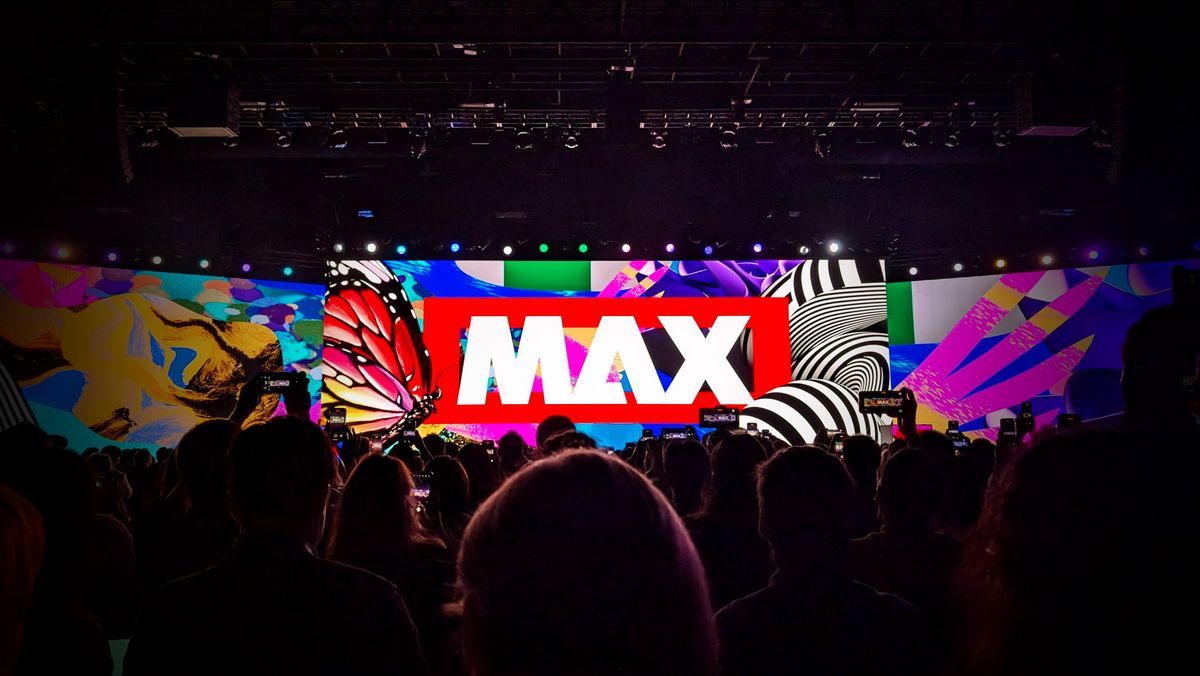 Audience gathered around a large screen with illustrations surrounding a large Adobe MAX logo