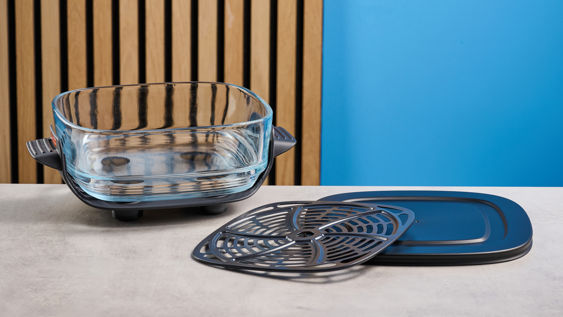 the kismile roasti air fryer with a glass cooking container photographed against a blue and wood background, showing the heating element lid