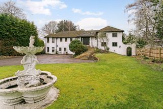 The front of a house has a large garden and driveway and fountain