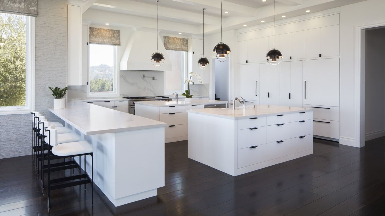 A modern white kitchen with dark floors and black pendant lights