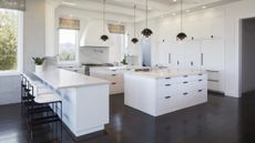 A modern white kitchen with dark floors and black pendant lights