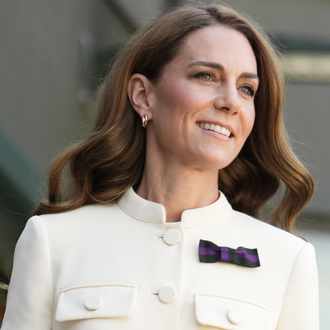 Kate Middleton wearing a white blazer with a purple bow pin and smiling