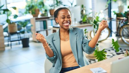 A woman celebrates at her desk in the office.