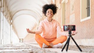 Woman vlogging while practicing lotus position outdoors