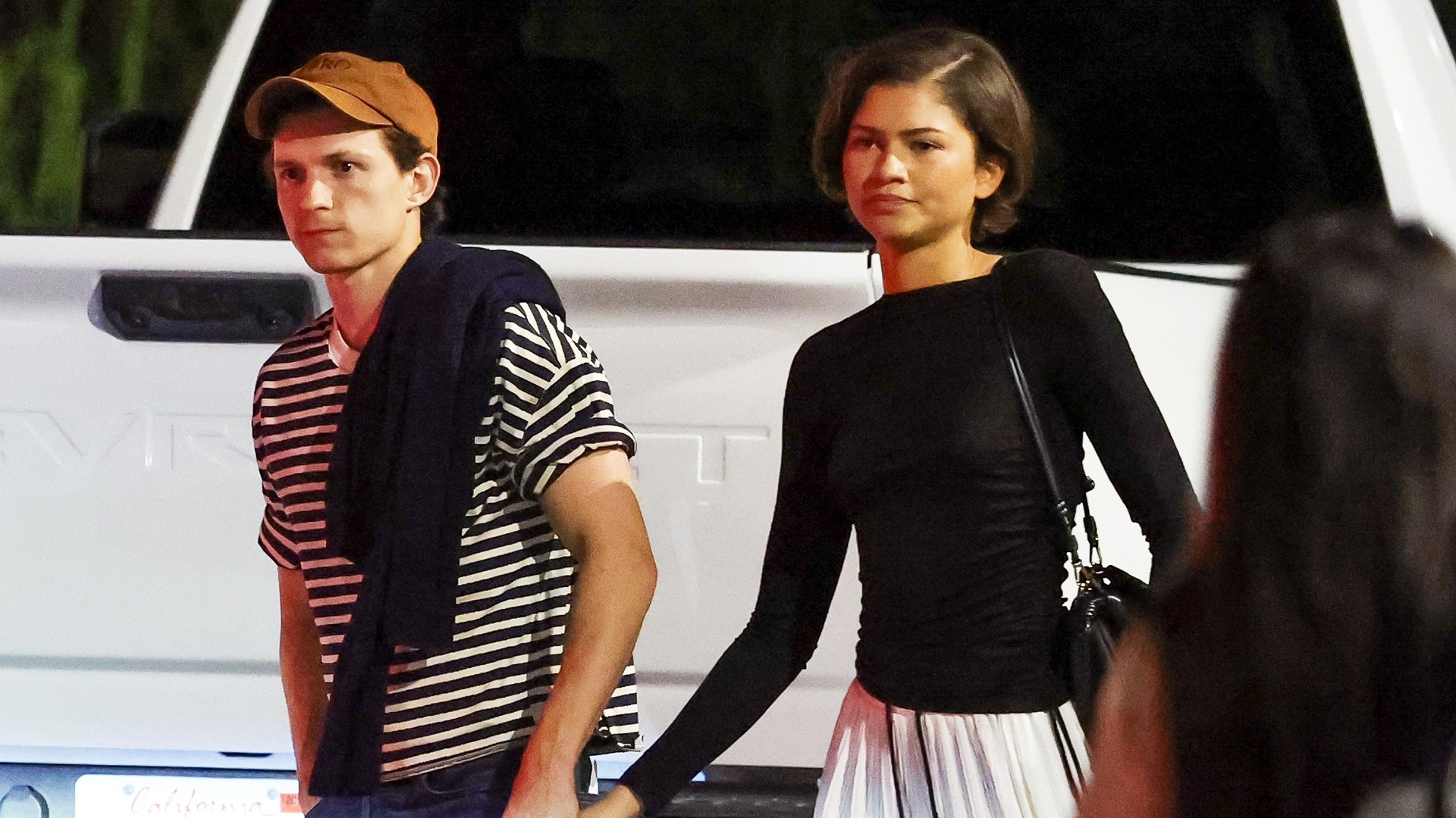 Tom Holland with Zendaya wearing a black top, white billowy pants, and black shoes