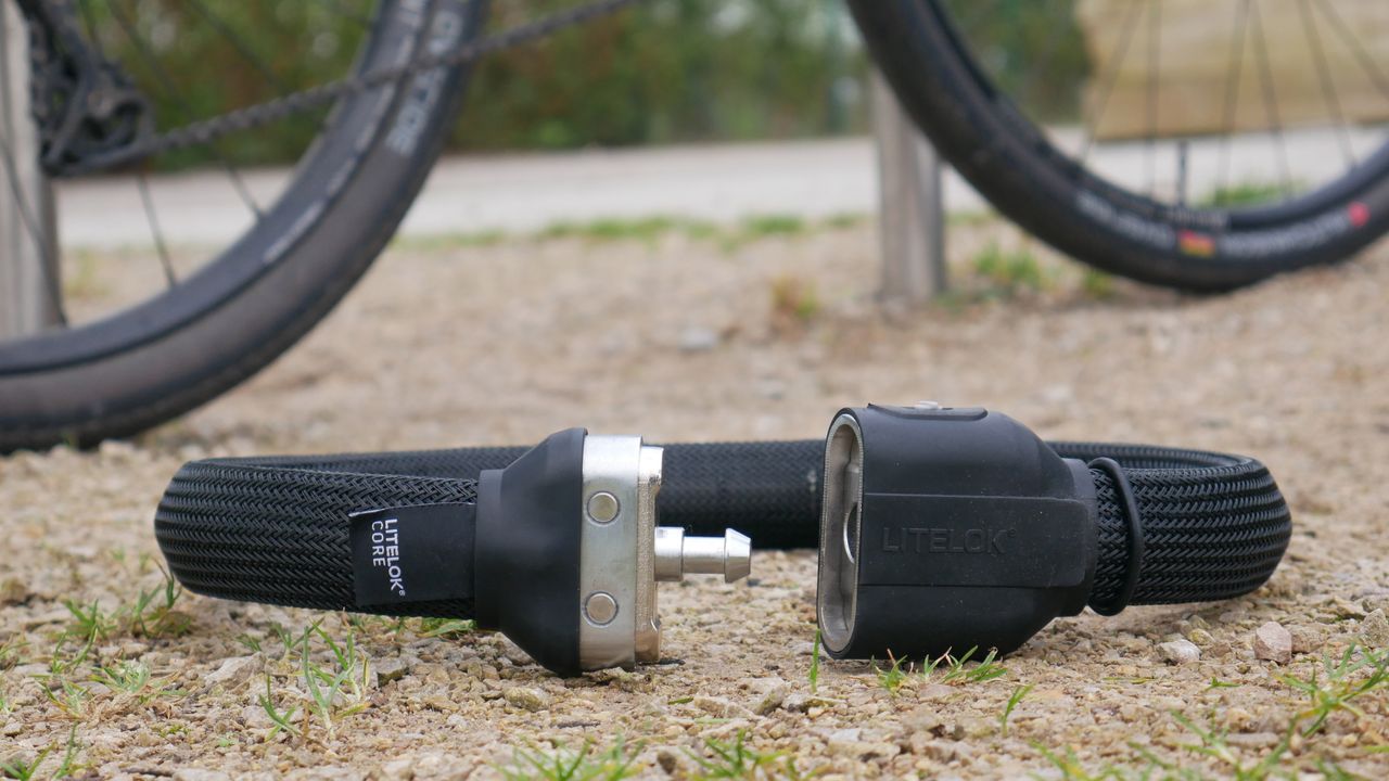 Litelok core plus resting on the ground next to a bike at a bike rack unlocked. A high security wearable bike lock