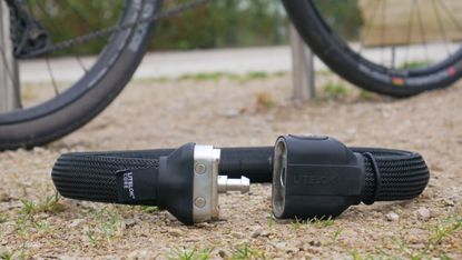 litelok core plus resting on the ground next to a bike at a bike rack unlocked. A high security wearable bike lock