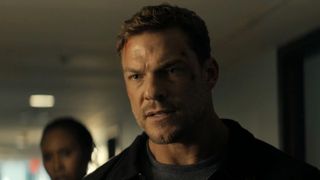 Alan Ritchson's Reacher standing in hotel hallway in a dark maintenance jacket and grey shirt, with scrapes on his forehead in Reacher Season 4