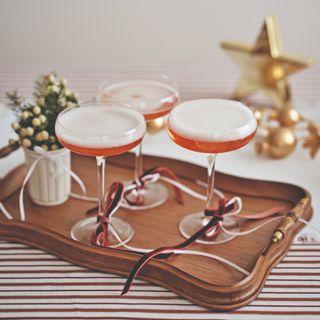 A tray with three Champagne coupes filled with drinks and decorated with red velvet bows at the stem