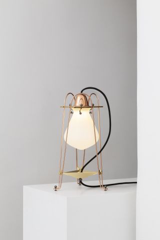 A lamp made of copper wire cage holding a large white bulb, created by Umberto Riva