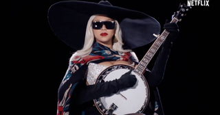 Beyonce wearing a cowboy hat and a cape while playing the banjo in a Netflix promotional commercial for her Christmas halftime show