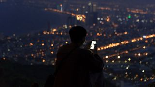 A Man Using His Smartphone with a View of City at Night
