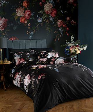 A black bedroom with floral wallpaper, a gray bed with black floral bedding, and a wooden floor