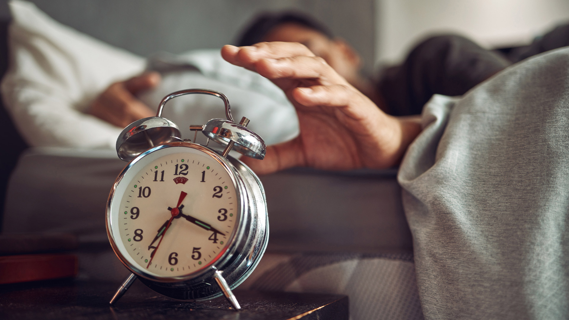 A person wakes up in the morning and reaches for the alarm clock