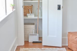 A white wooden closet with a broom and dustpan, lint roller and spray bottles, part of the Muji and Airbnb holiday home essentials kit