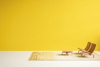 A wide room with bright yellow wall and white floor, with a pair of modernist chairs and coffee table placed onto a yellow and beige area rug by David Thulstrup