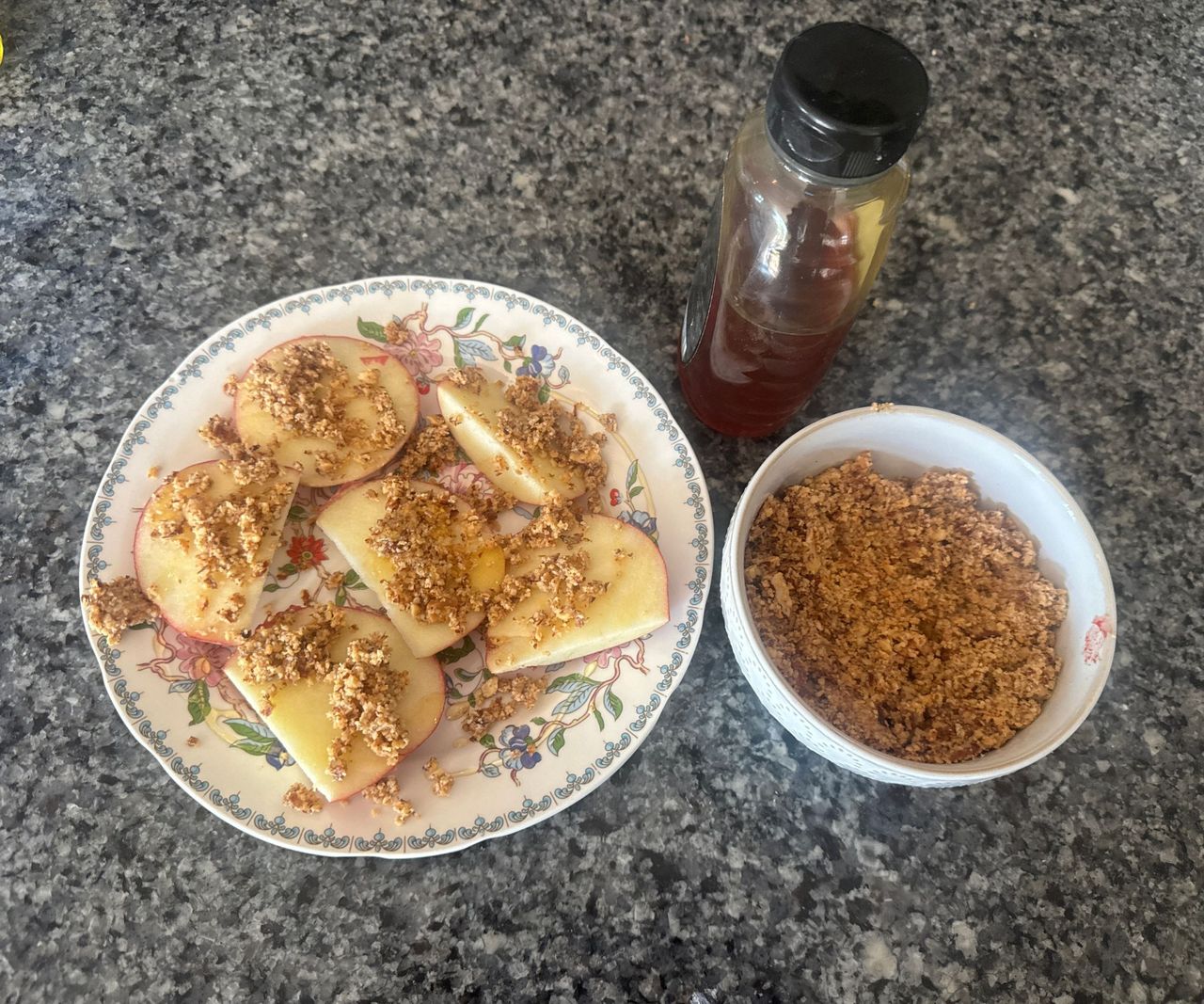 A plate with sliced apples and nut butter spread on them, beside a bowl of nut butter and a container of honey.