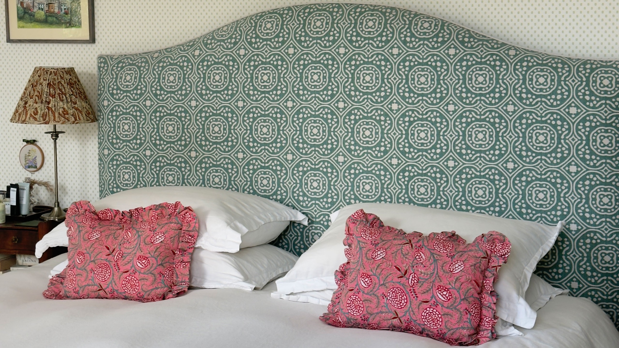 Bed with upholstered patterned green headboard and two pink floral decorative pillows