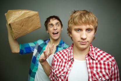 One crazy looking man about to pop a paper bag next to an angry looking man's ear. 