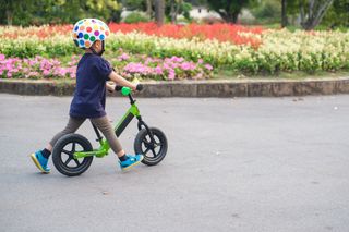 toddler boy child wearing safety helmet learning to ride first balance bike in sunny summer day
