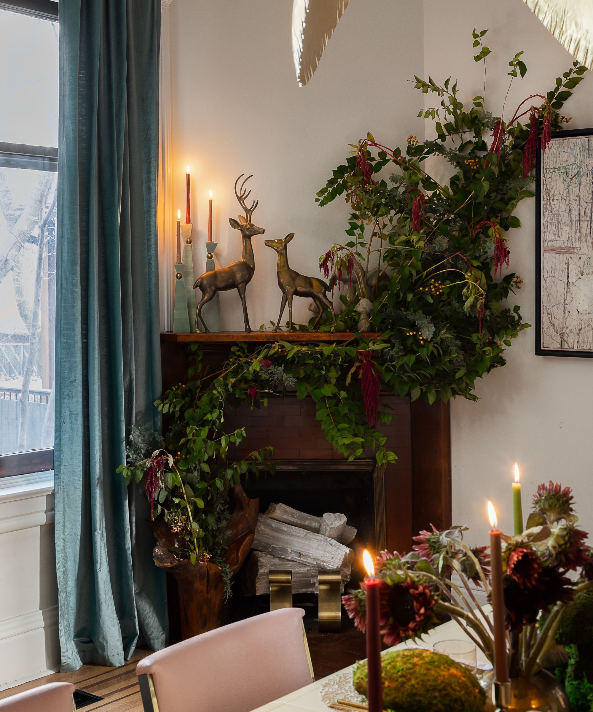 Fireplace mantel decorated with lush green and red foliage, tall candlesticks, and two bronze deer sculptures