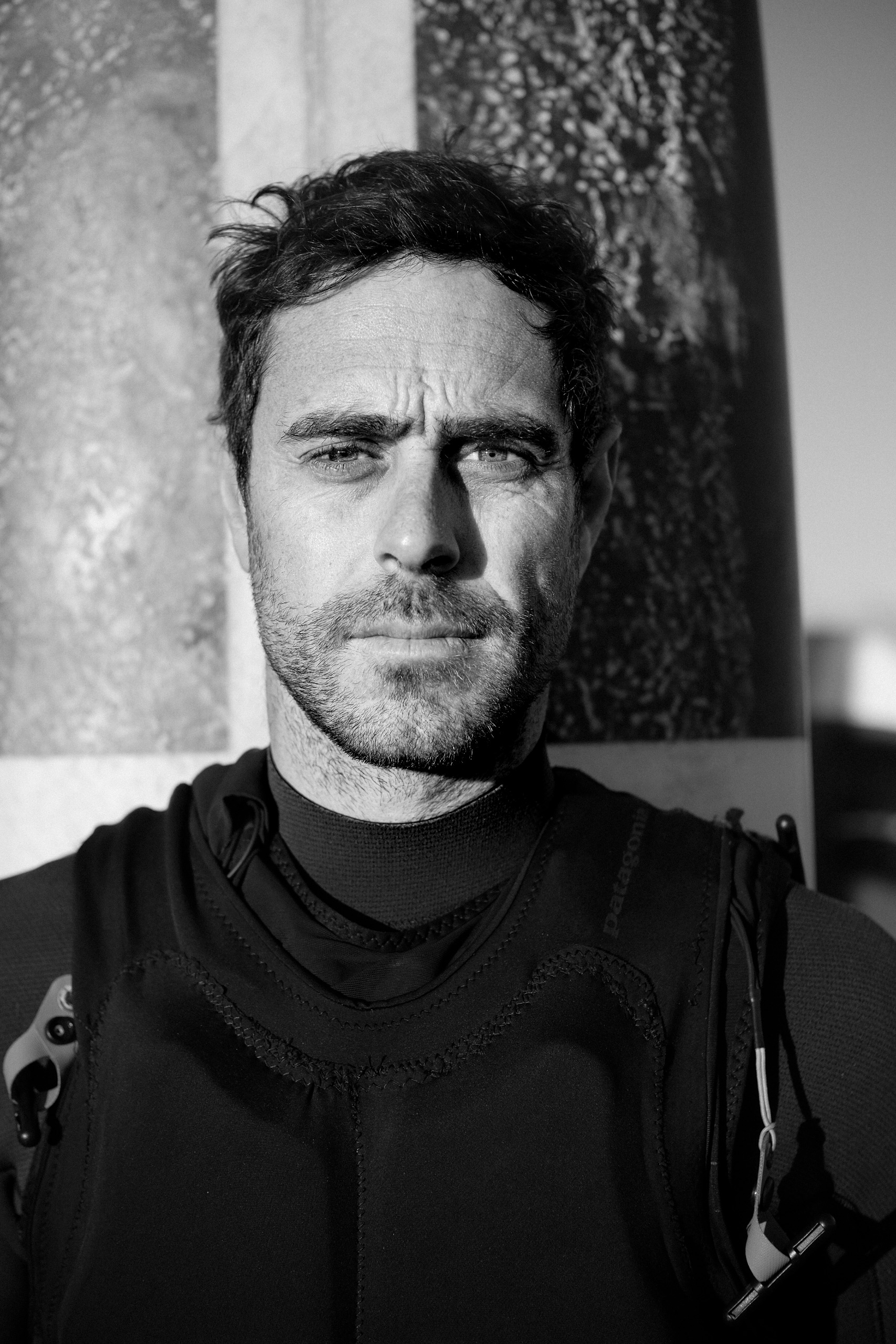 Black-and-white portrait of Tom Butler in front of his surfboard