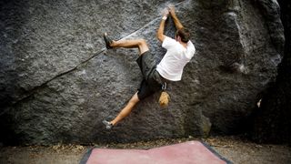 A climber performs a heel hook while bouldering over a red crash pad