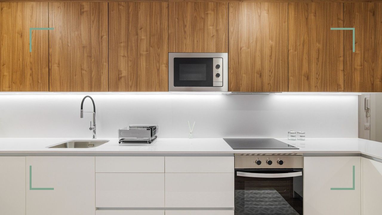 a modern, minimalist kitchen with white countertops, and wooden cupboards above, with a microwave built-in to consider things you should never put in a microwave