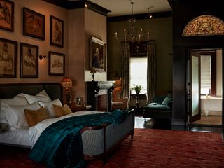 A room with artwork on the walls, a stained glass window, and a blue velvet blanket on a white bed at The Maker hotel in Hudson, New York