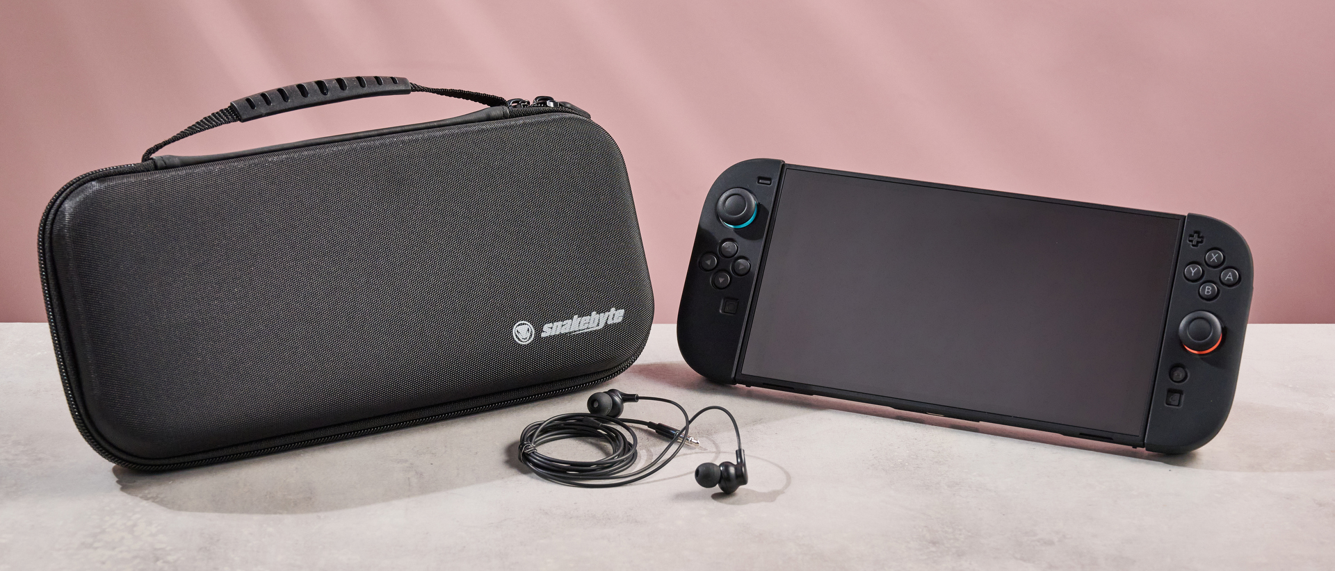The Nintendo Switch 2 sitting side-by-side with the Snakebyte Starter Kit S2 case; in between them sits the Snakebyte wired earbuds.