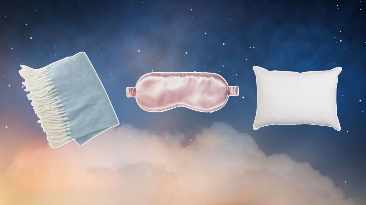 Bedding items including a baby blue throw blanket, a pink sleep mask, and a white standard pillow on a blue, starry, and cloudy background.