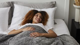 Mela Original Weighted Blanket review: a woman with brown and red curly hair smiles in bed as she relaxes beneath the Mela Original Blanket
