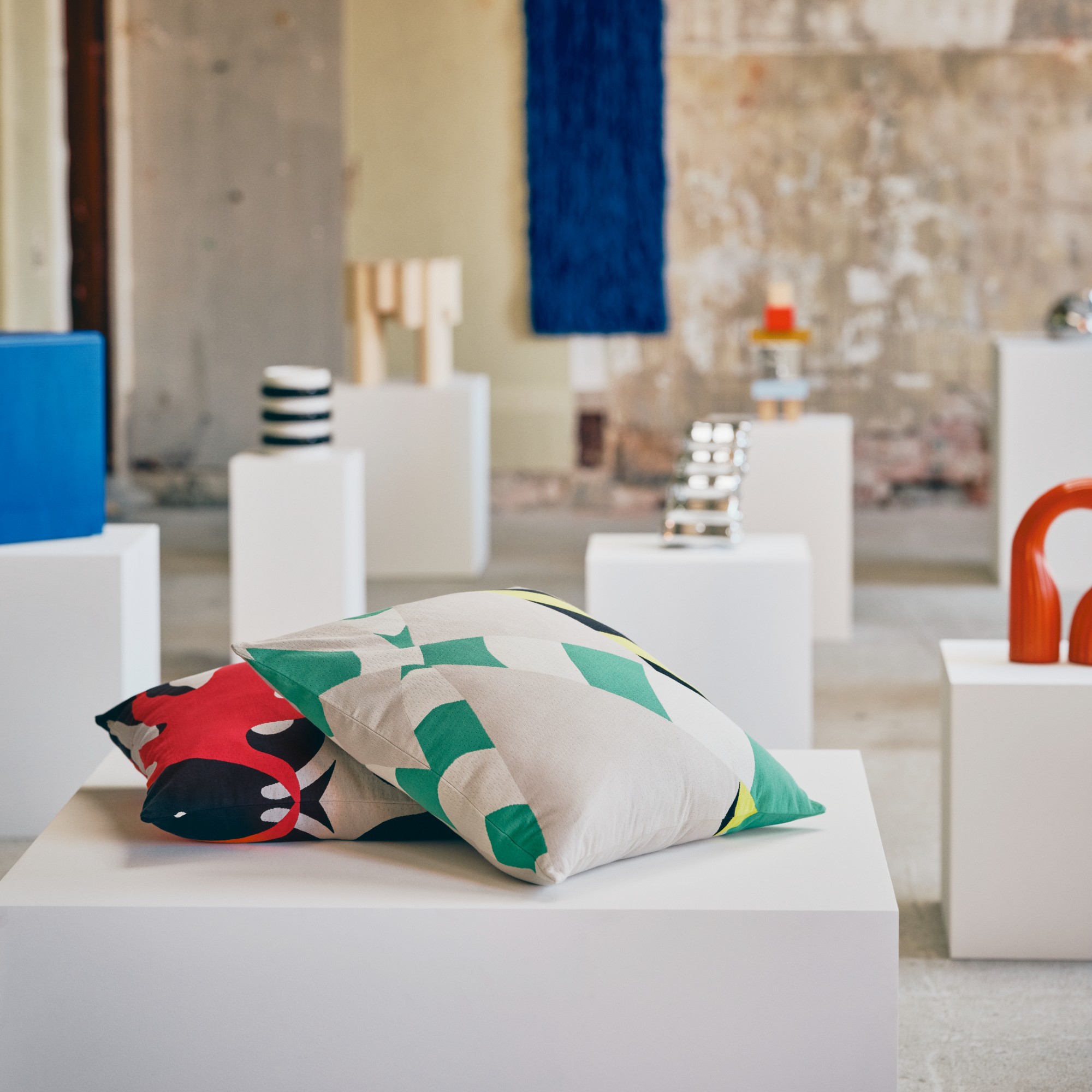 An industrial-style space filled with pillars displaying pieces from the IKEA KONSTRUNDA collection with the printed cushions at the front