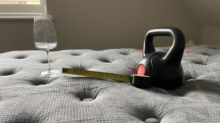 A wine glass, weight and tape measure on the Zoma Boost mattress