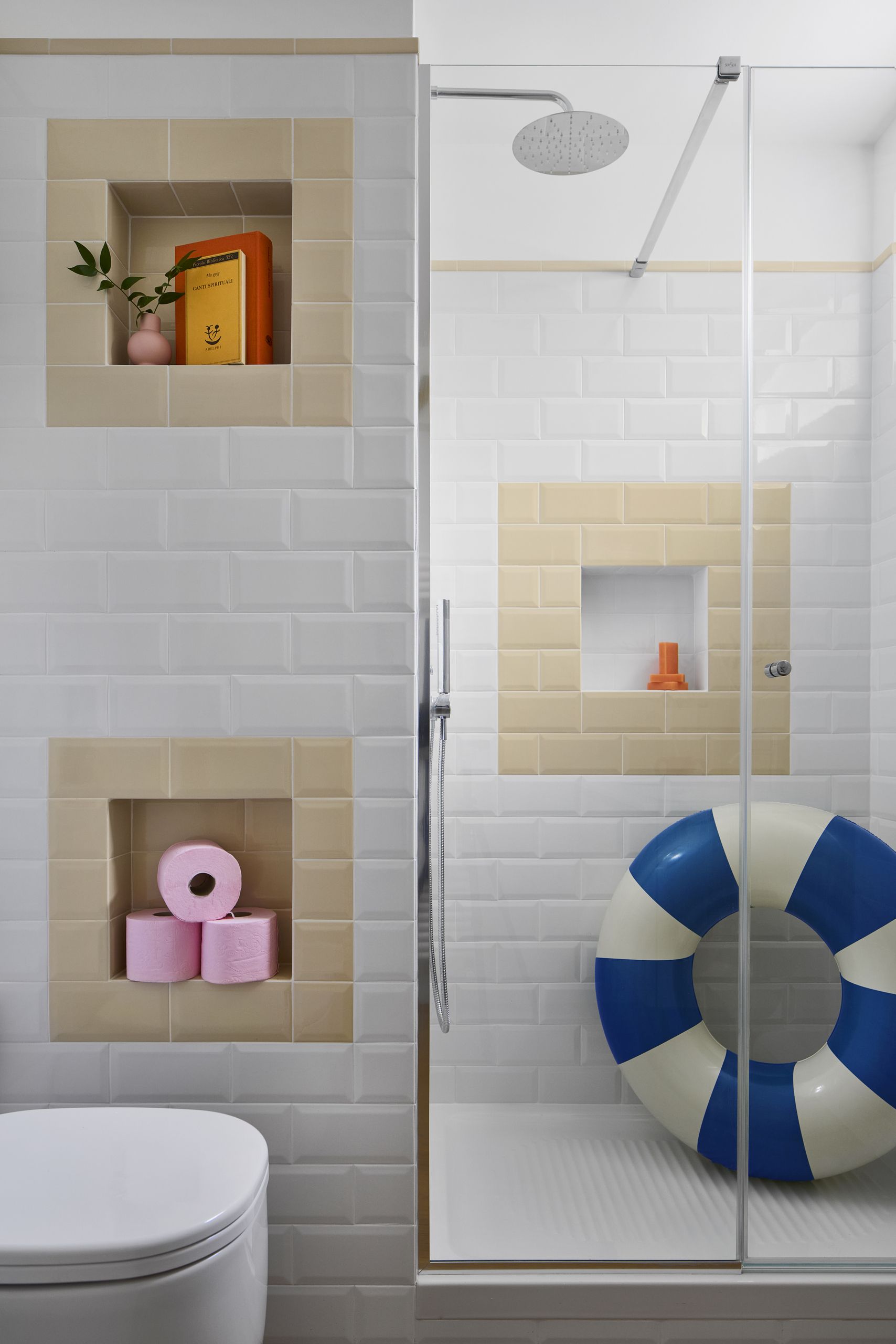 A small white bathroom with tiled walls and light cream tile nooks, a shower cubicle with a blue and white pool ring, a white toilet, and a set of pink toilet rolls