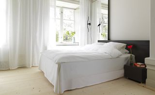 Hotel Skeppsholmen, Stockholm. A hotel room with a white double bed, a black side table, a floor lamp and a large window with white curtains.