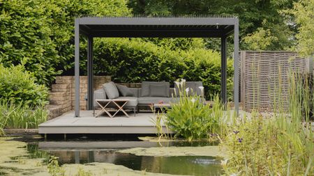 Pergola with retractable roof on a raised platform by a large pond in a garden