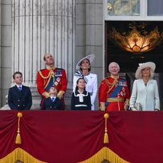 A photo of the royal family in dresses and military uniforms standing on the balcony at Buckingham Palace during Trooping the Colour looking up at the sky