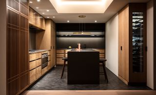 A fitted kitchen made with wood and a dark island with two stools.