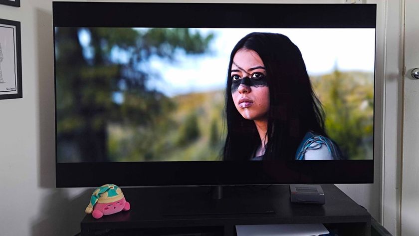 LG OLED G4 gaming TV sitting on black TV bench with sleeping Kirby plush on left and mini PC on right featuring clip from Prey with main character Naru on screen.