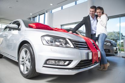 Man looking at new car with red bow with girlfriend in car dealership 