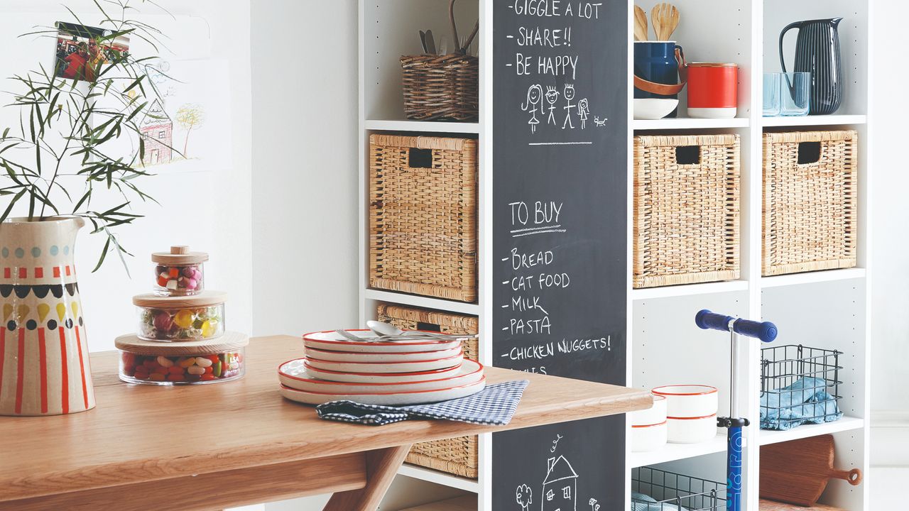 Dining area with storage shelves and baskets in the corner, blackboard panel, white walls and white painted floorboards