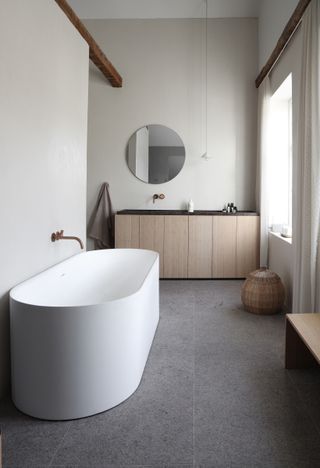 A large bathroom with a curved bath, brass wall taps and a circular mirror