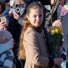 Princess Charlotte wearing a tan coat and holding yellow roses