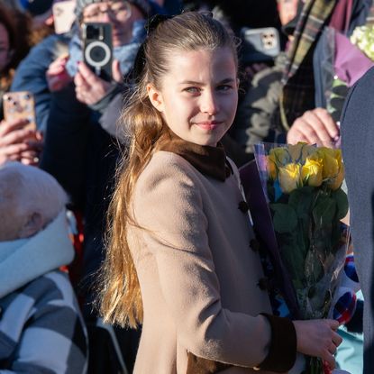 Princess Charlotte wearing a tan coat and holding yellow roses