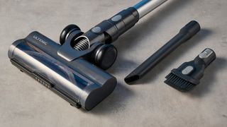 a modern-looking sleek shiny vacuum cleaner with light grey components on a carpet in front of a blue background