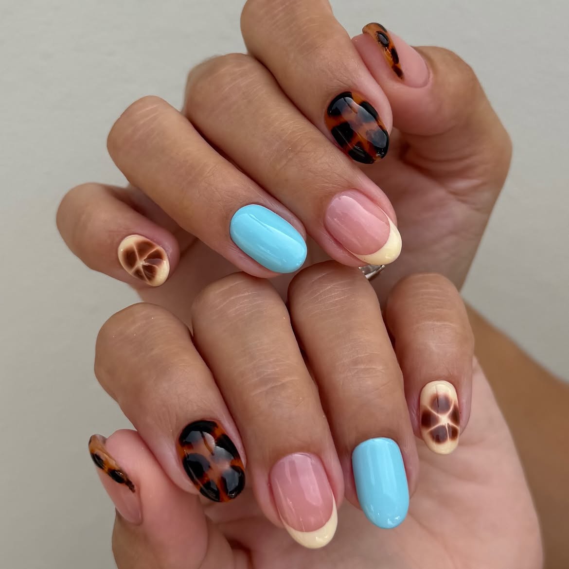 Mismatched almond nails featuring tortoiseshell print, glossy pool blue polish, and blooming yellow florals