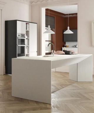 A rectangular white kitchen island with a mirrored base, a black and silver fridge behind it and an open door frame and white walls