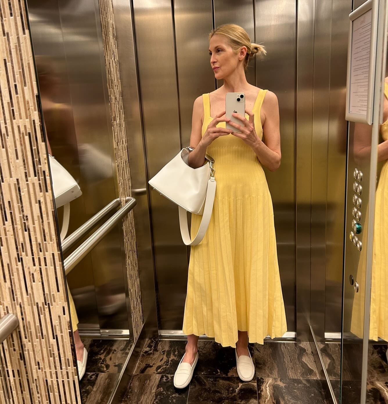 Woman in elevator wears yellow dress, white shoes and white bag