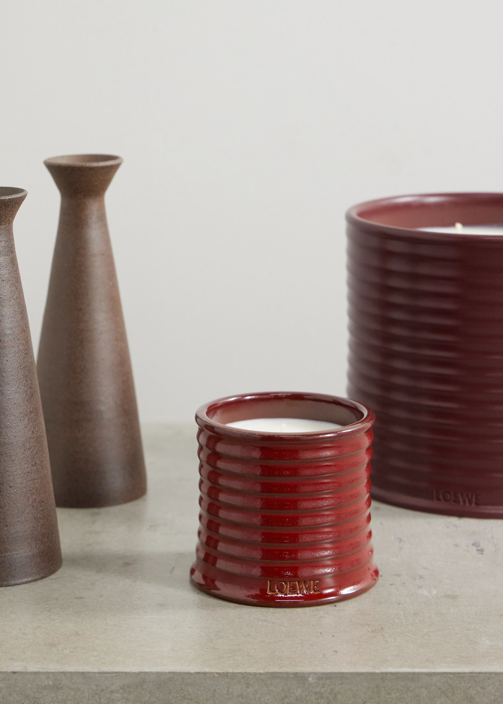 A pair of red ribbed candles by vases